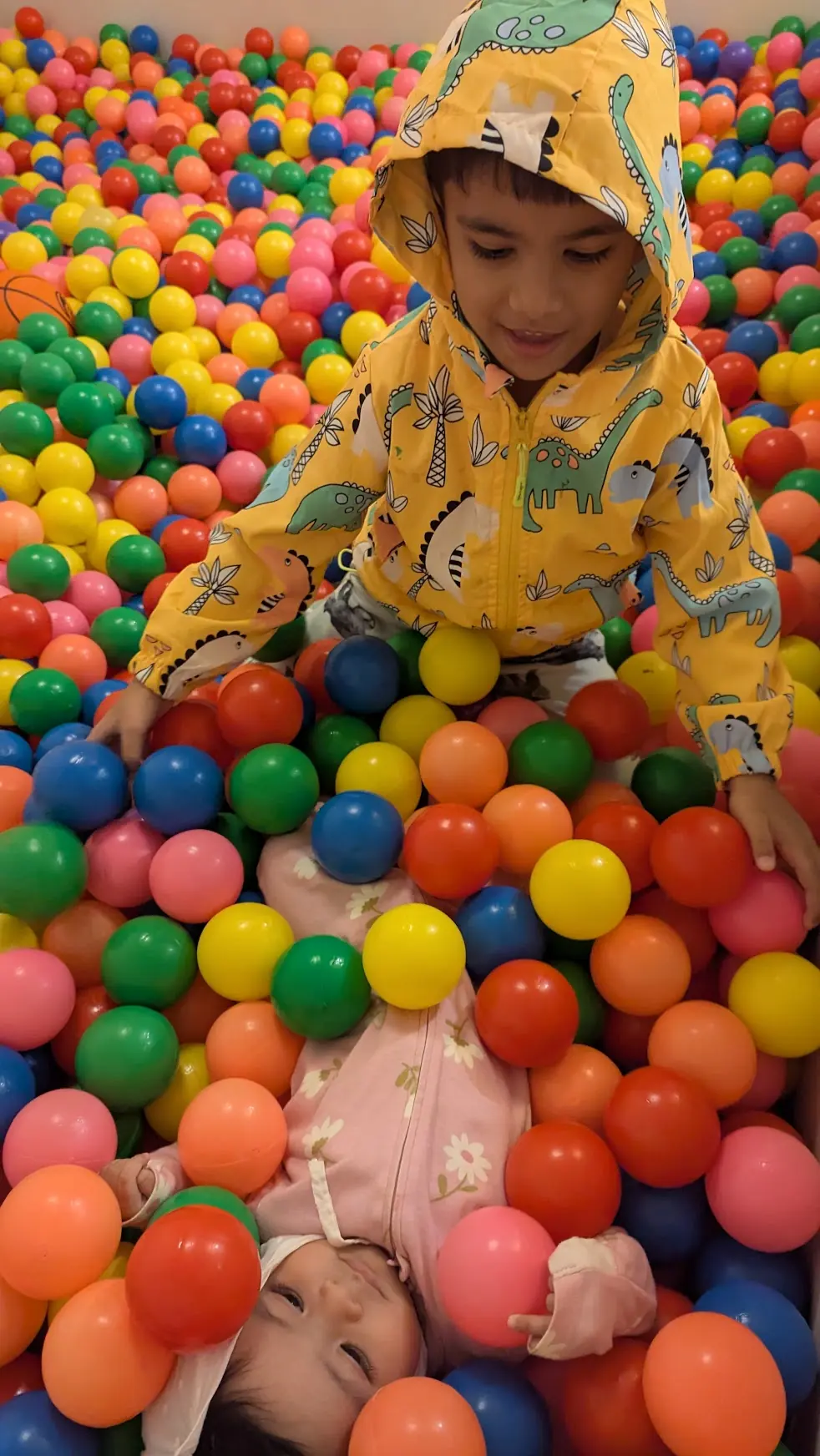 A boy in a yellow raincoat playing in a ball pit