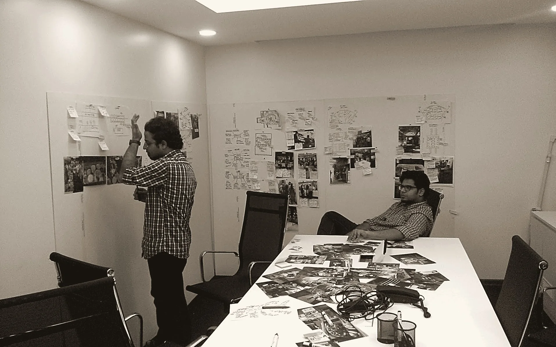 Two members of the Tinyowl team at a wall of research notes and photos, with printouts spread across the table
